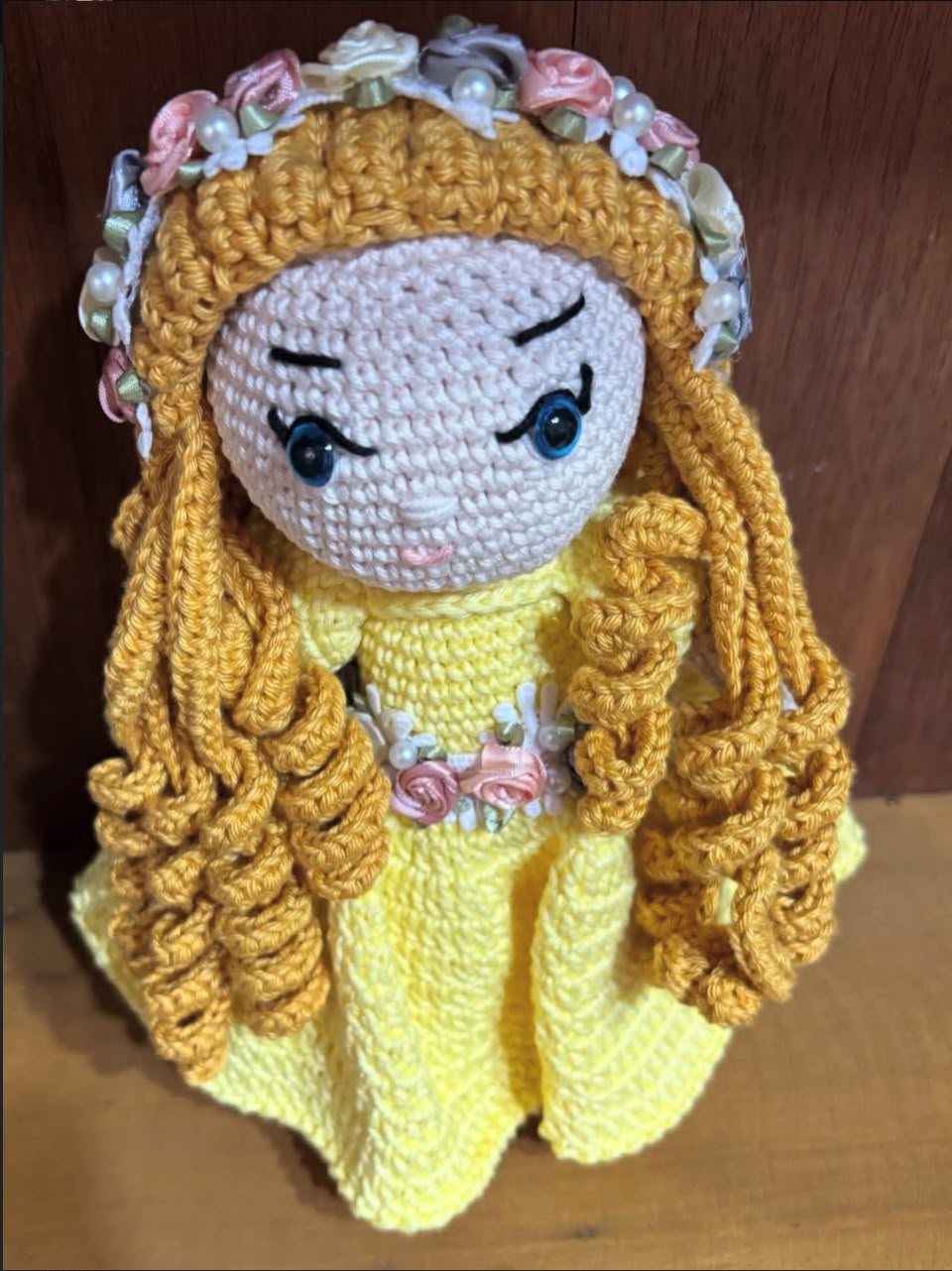 Boneca de crochê de vestido amarelo, cabelos dourados cacheados e tiara de rosas com pérolas.