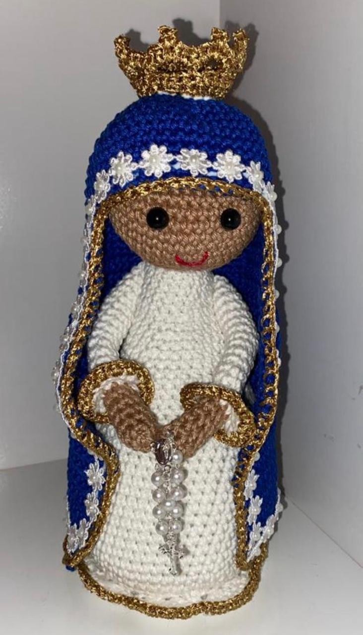 Imagem de Nossa Senhora em crochê em tons morenos, manto azul com florzinhas brancas, coroa dourada trabalhada e rosário na altura da cintura.